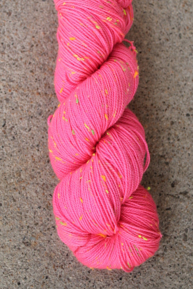 Skein of coral pink yarn with yellow specks on a concrete surface