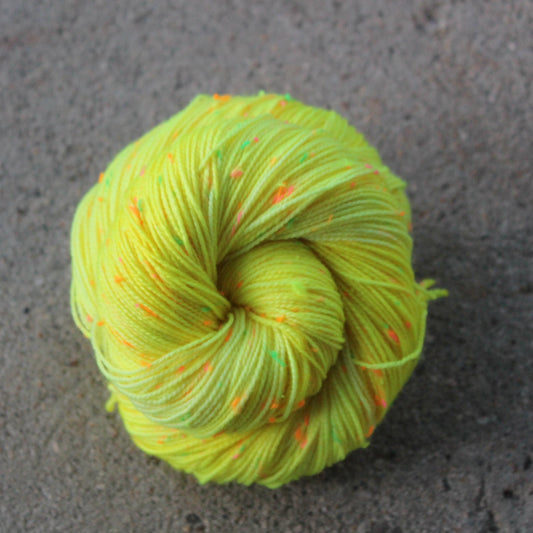 Neon yellow skein of yarn with orange speckles on a gray concrete surface